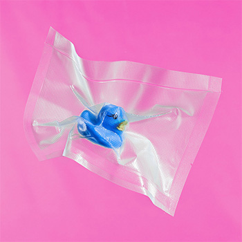 Konzeptfotografie einer vakuumierten blauen Badeente vor pinkem Hintergrund.