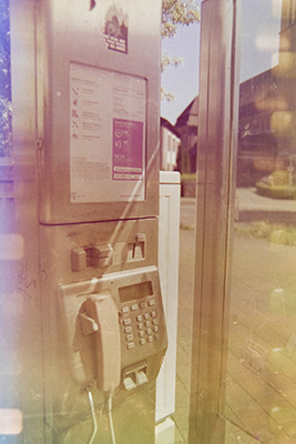 Hochformatige Aufnahme einer Telefonzelle, an den Bildrändern sind helle rechteckige Lichtflecken sichtbar, verursacht durch den Filmstreifen.
