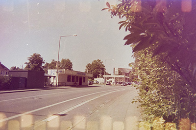 Querformatige Straßenansicht mit Tankstelle und Dönerladen. Gegenüberliegend grüne Büsche. Oben und unten sind helle rechteckige Streifen vom Film zu sehen.