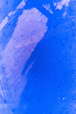 Blau eingefärbte diagonale Aufnahme von quadratischem Pflasterstein. Auf den Steinen zeichnen sich schattige Umrisse von Bäumen ab.