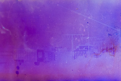 Querformat. Eine angedeutete Stadtlandschaft, getaucht in ein Farbspektrum aus Lila, Blau und Pink. Die Konturen verschwimmen fast vollständig in der atmosphärischen Farbgebung.