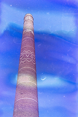 Hochformat. Ein hoher Industrieschornstein vor klarem blauen Himmel. Ein bläulicher fleckiger Schimmer liegt über dem gesamten Bild.
